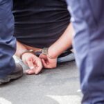 Midsection Of Prisoner Sitting On Street Surrounded With Police Force